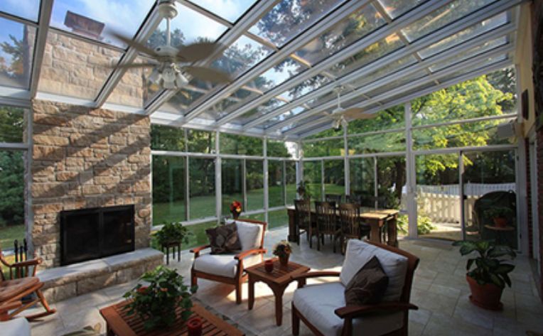 Interior of a sunroom with a dining room table, outdoor chairs, a coffee table, and a fireplace with a ceiling fan overhead.